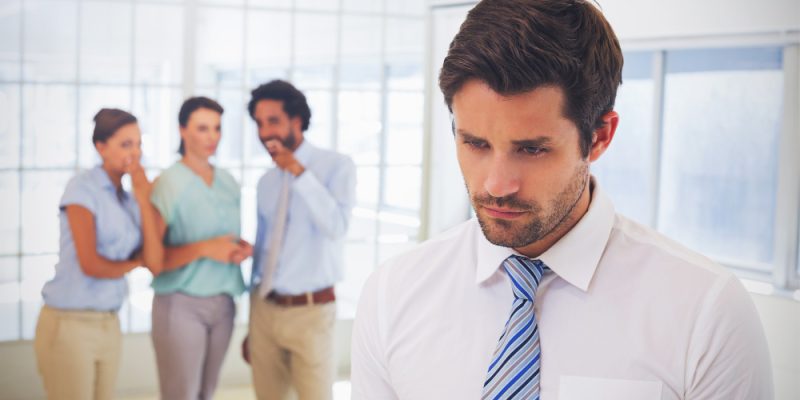 colleagues-gossiping-with-sad-businessman-in-foreground
